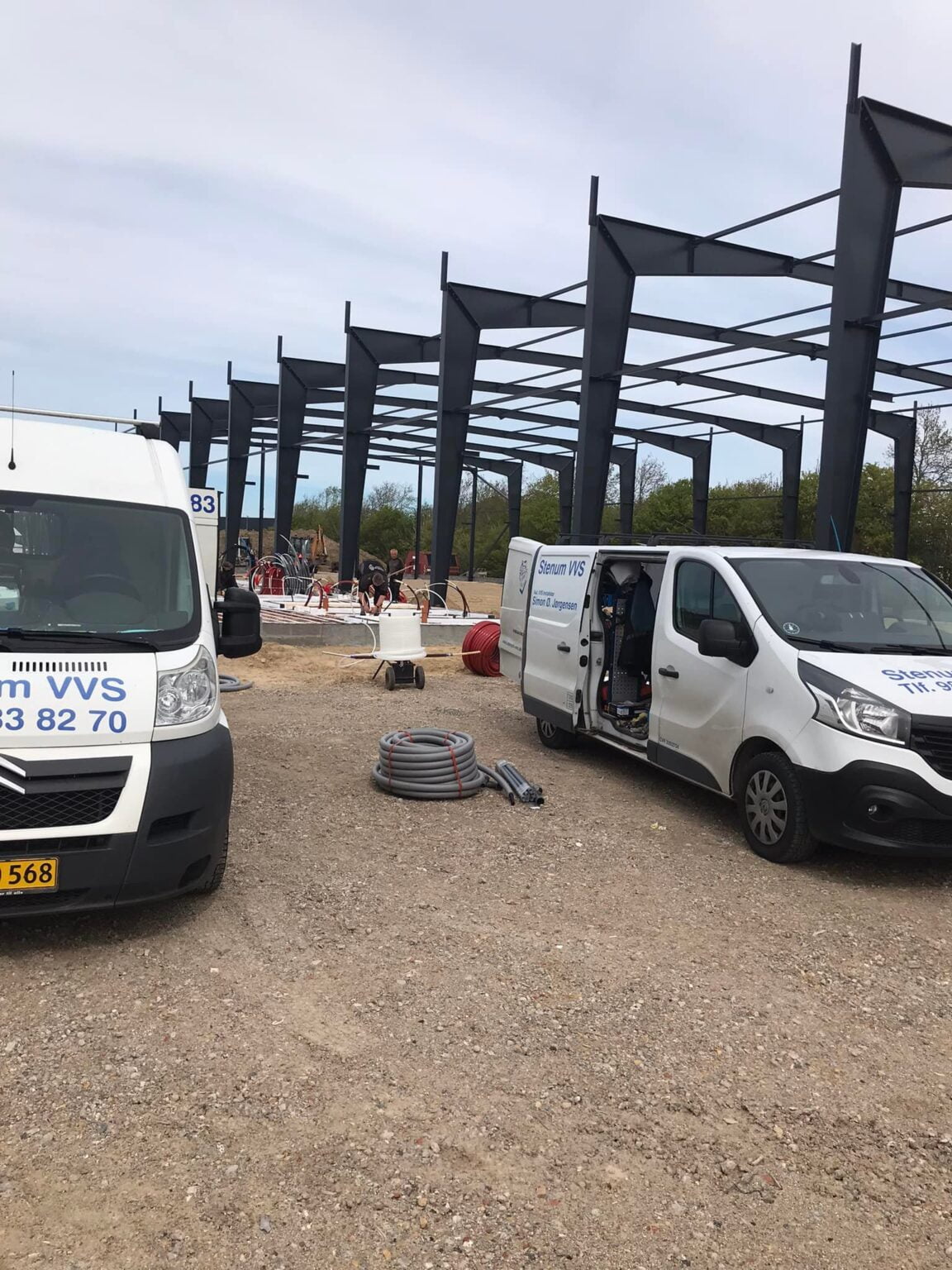 VVS-firmabiler ved byggeplads med stålkonstruktion