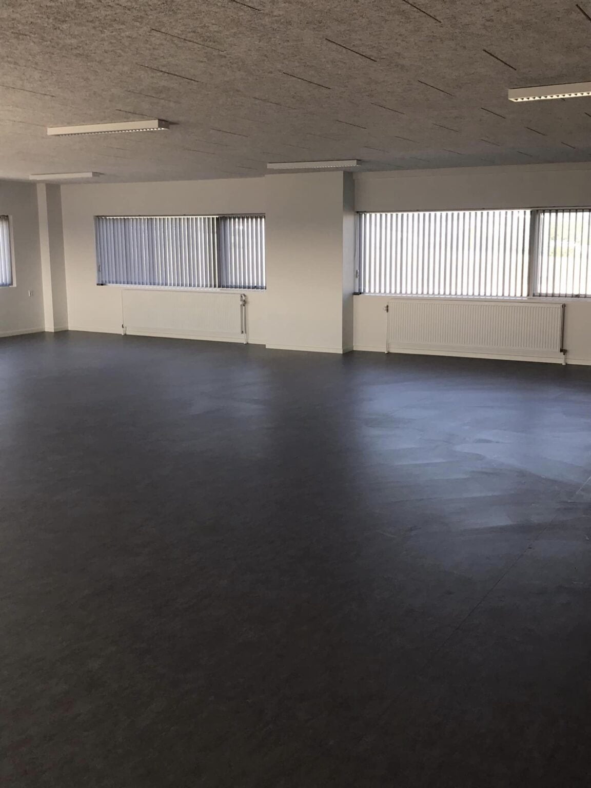 Tomt kontorlokale med store vinduer og grå gulve