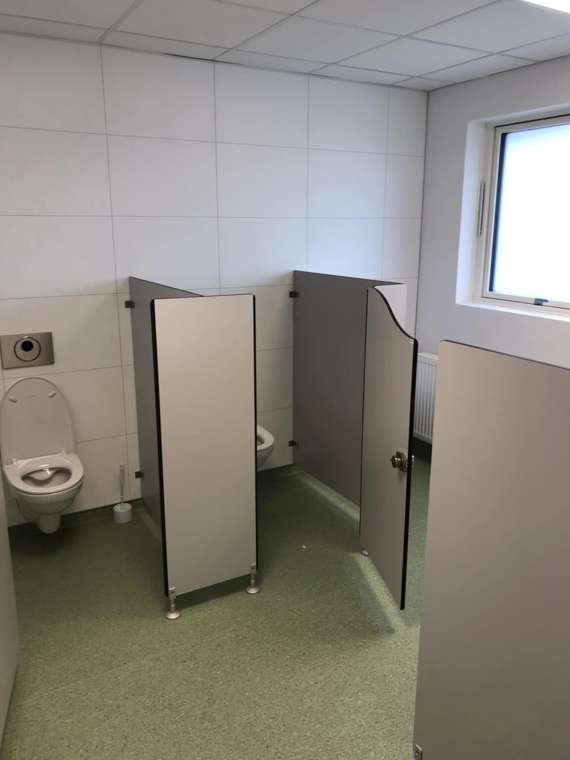 Offentligt toilet med to båse og hvidt interiør