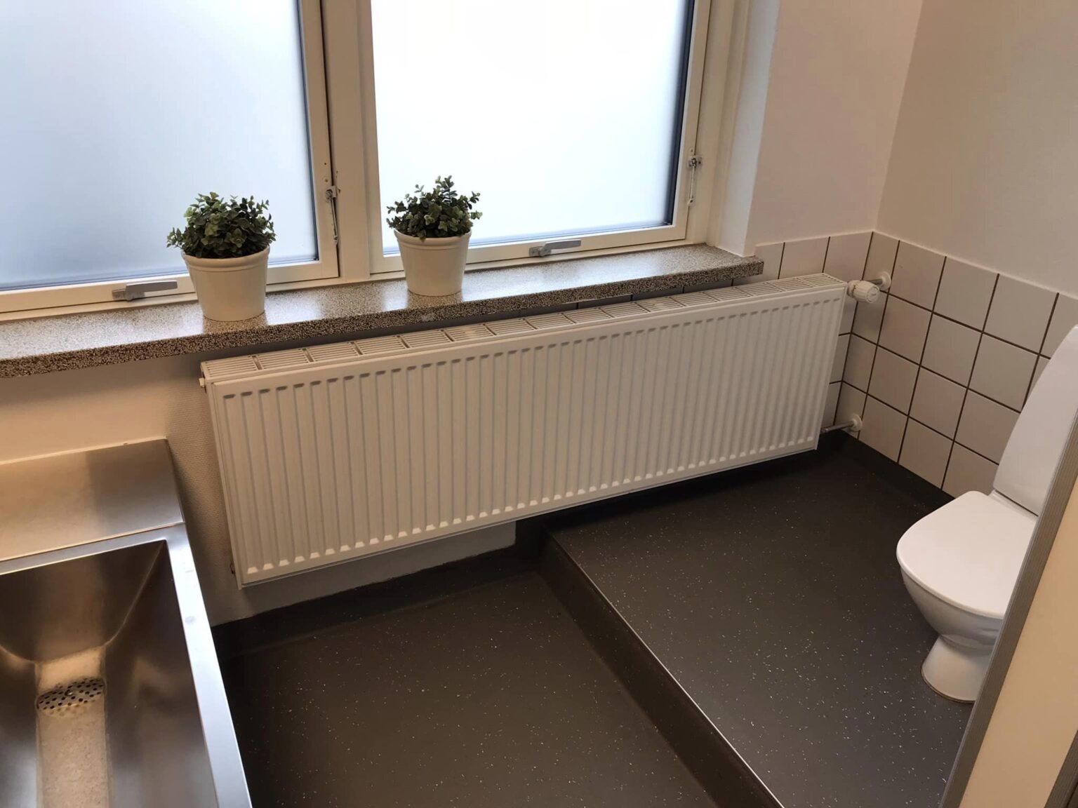 Lyst badeværelse med toilet, håndvask og planter ved vindue