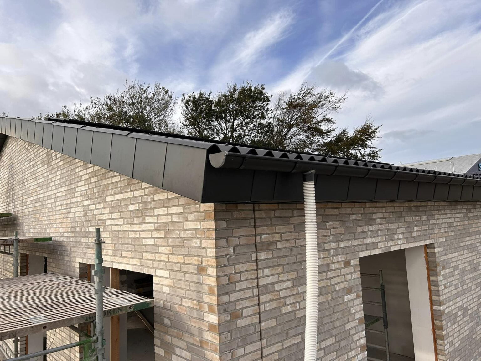 Nyt murstenshus med sort tagrende og stillads