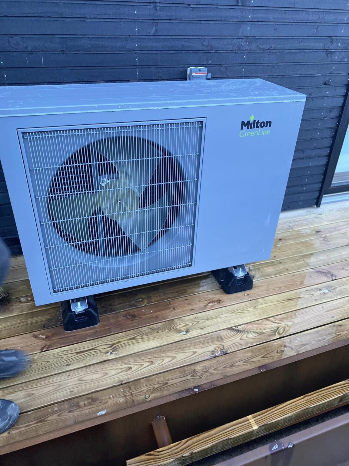 Udendørs varmepumpe på træterrasse foran sort væg